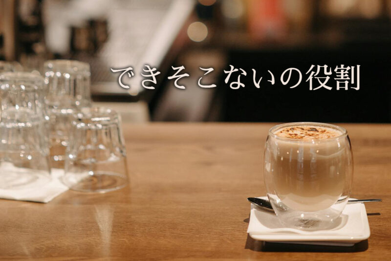 木製カウンターに置かれた二重ガラスのカフェラテと積まれたグラス